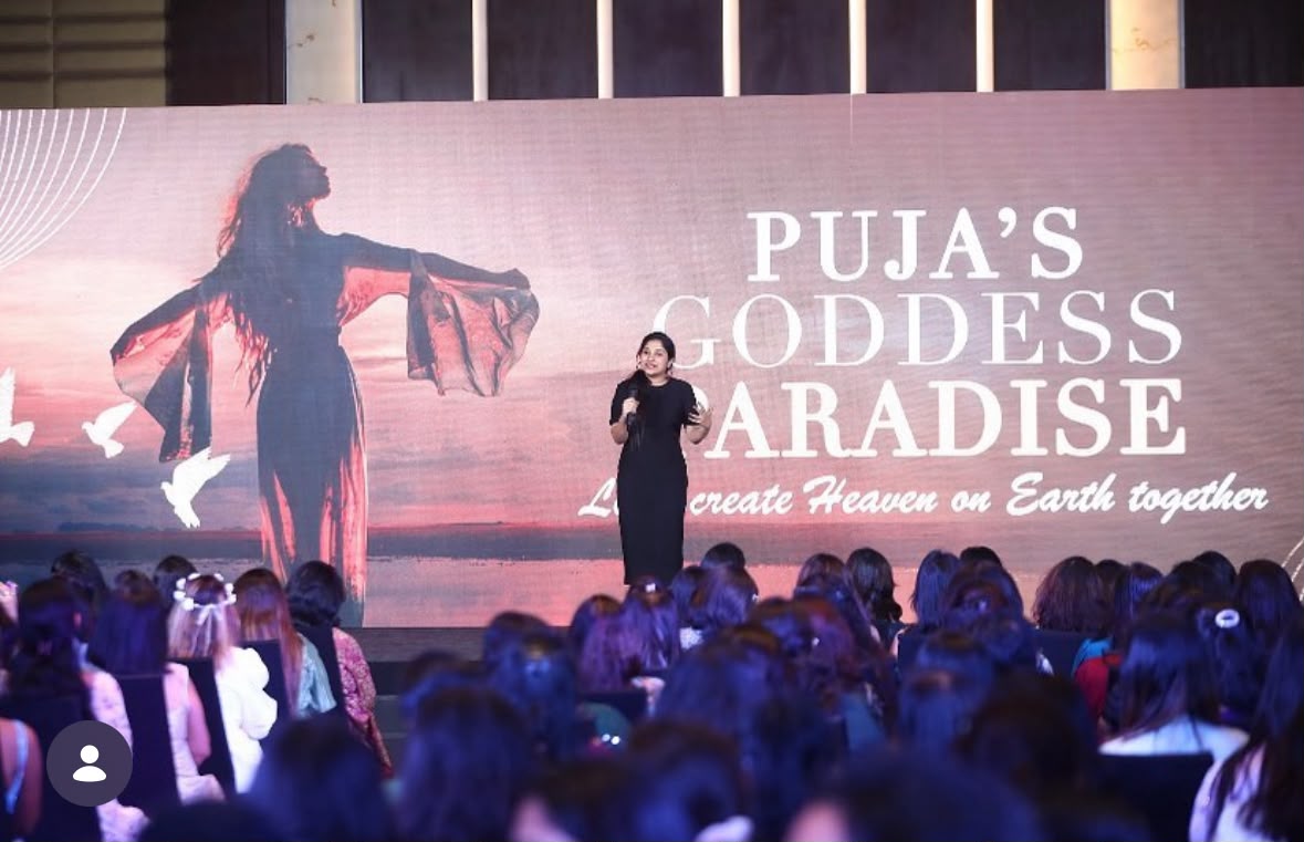 Madhu speaking on stage to a room full of women